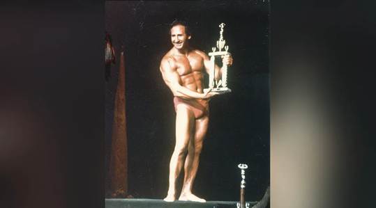 Andrew Bostinto holding a trophy form a bodybuilding competition he won during his younger years